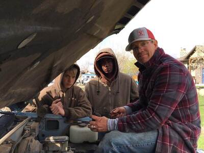 Dad working on a farm truck transmission with the boys